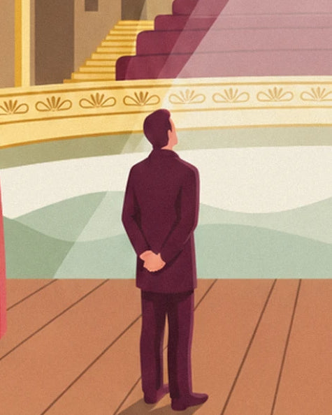 The man in a burgundy suit, hands behind his back, on stage facing the golden balcony