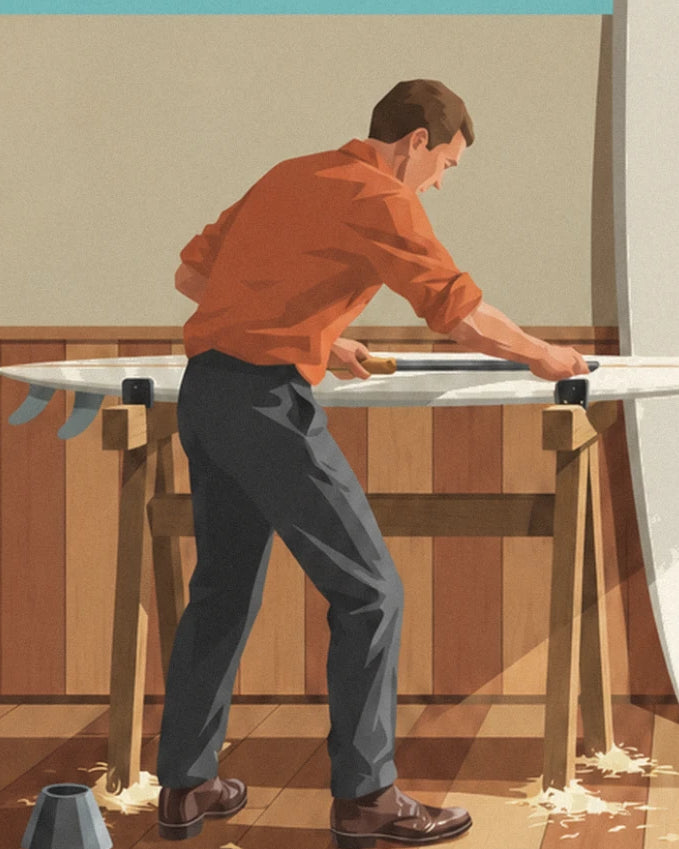 The surfboard shaper in an orange shirt planing a board on 2 trestles, with shavings on the floor
