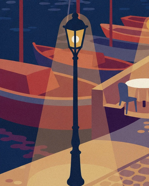 The black street lamp and its golden glow in front of the harbour's red boats