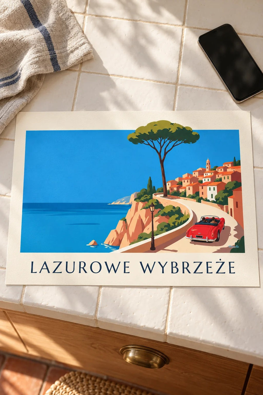 Plakat czerwony kabriolet na nadmorskiej drodze Lazurowego Wybrzeża: leżący na stole